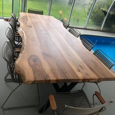 a wooden table with chairs around it in front of a swimming pool and large windows