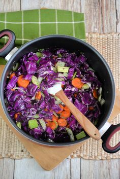 a pot filled with cabbage and carrots on top of a wooden cutting board next to scissors