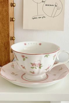 a cup and saucer sitting on top of a white table next to a painting