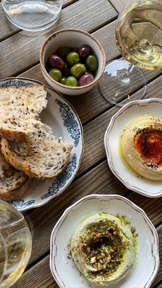 an assortment of food and wine on a wooden table with two glasses of white wine