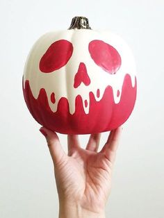 a hand holding up a red and white painted pumpkin