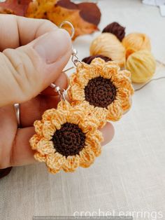 a hand holding two crocheted sunflower earrings