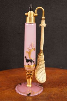 a pink glass bottle with a golden handle next to an umbrella on a wooden table