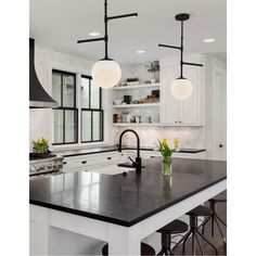 a large kitchen with black counter tops and white cabinets, along with two pendant lights hanging from the ceiling