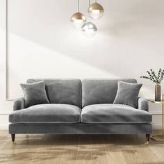 a gray couch sitting on top of a hard wood floor next to a vase with flowers