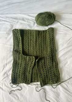 a green knitted scarf laying on top of a bed next to a ball of yarn