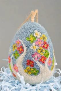 an egg decorated with flowers and leaves on top of shredded blue fabric, sitting on a table