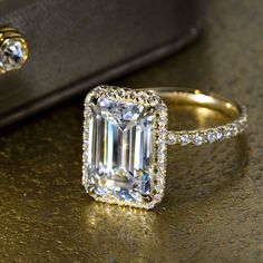 an emerald colored diamond surrounded by diamonds on top of a gold table next to a black bag