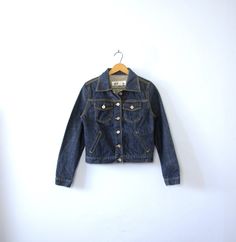 One vintage 1990's dark denim jacket, Express jean jacket, women's size small - Pointed collar. - 6 button closures going down the center front of the jacket. - 2 chest pockets with flaps and button closures. 2 slide pockets on the front of the jacket. - 1 button on each wrist cuff. - 2 tabs on the back of the waistband with 2 adjustable buttons. - Shorter, feminine fit through the torso. - Thick 100% cotton. Not broken in. - Color scheme: dark blue denim. Silver toned hardware. | CONDITION | A+ Vintage Dark Wash Button-up Denim Jacket, Dark Wash Cotton Denim Jacket With Buttons, Vintage Dark Wash Outerwear For Spring, Dark Wash Denim Jacket With Buttons, Winter Fitted Denim Jacket With Button Closure, Fitted Dark Wash Denim Jacket For Fall, Fitted Denim Jacket With Button Closure For Winter, Fitted Winter Denim Jacket, Fitted Denim Jacket For Winter