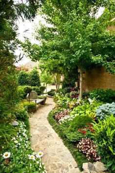 a garden with lots of plants and flowers on the side of it, along with a stone path