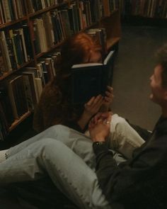 a man and woman sitting on the floor in front of bookshelves holding hands