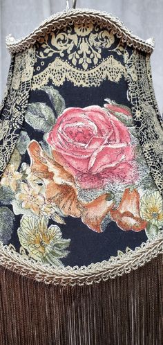 a close up of a lamp shade with a rose on it and tassels