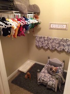 a baby's crib in the corner of a room with clothes hanging up