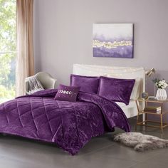 a bed with purple comforter and pillows in a room