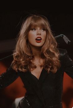 taylor swift performing on stage with her hands in the air, wearing a black suit and red lipstick