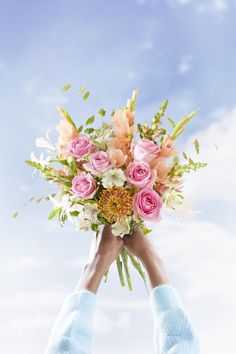 a person holding a bouquet of flowers in their hands against a blue sky with clouds