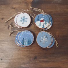 three ornaments are hanging from twine on a wooden table, one is decorated with snowflakes and the other has an ornament