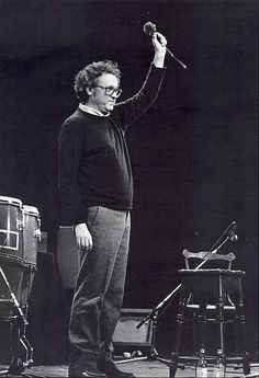 a man standing on top of a stage holding a microphone in one hand and an instrument in the other