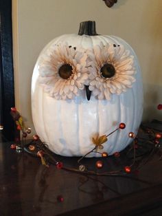 a white pumpkin decorated with flowers and an owl's face on top of it