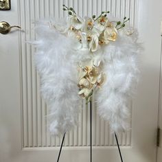 an arrangement of flowers and white feathers on a stand in front of a door,