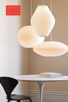 three white lamps hanging from the ceiling above a table with two chairs in front of it