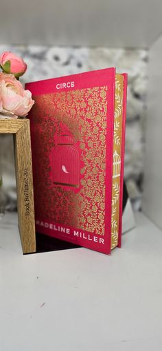 a red book sitting on top of a table next to a vase filled with flowers