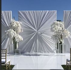 two tall vases filled with white flowers sitting on top of a table next to chairs