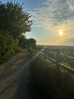 the sun shines brightly through the clouds over an empty country road near a fence