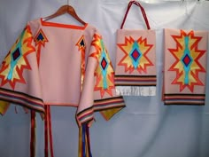 three pieces of colorful clothing hanging on a wall next to a bag and two bags with tassels