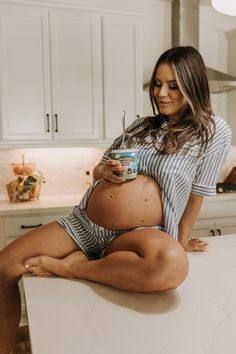 a pregnant woman sitting on top of a kitchen counter