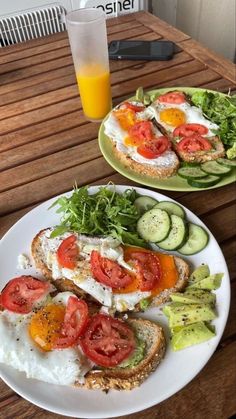 two plates filled with food sitting on top of a wooden table next to a glass of orange juice