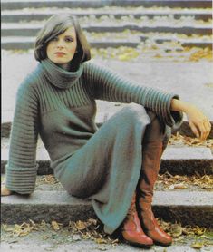 a woman is sitting on the steps wearing boots and a green knitted turtle neck sweater