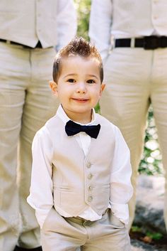 a young boy in a suit and bow tie standing next to two other men wearing white pants