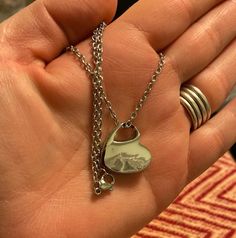 a hand holding a silver necklace with a heart on it