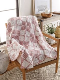 a white and red blanket sitting on top of a wooden chair next to a window