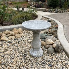 a birdbath sitting on top of a gravel covered ground next to rocks and trees