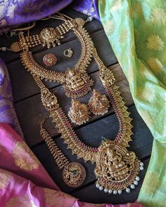 an assortment of gold jewelry on display in front of a purple and green saree