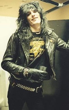 a man with long hair wearing a black leather jacket and holding his hands out to the side