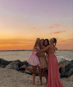 three girls are hugging on the beach at sunset