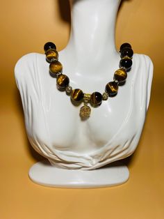 Add a touch of elegance to your outfit with this stunning gemstone necklace designed for women. Featuring 16mm Tigers Eye gemstone beads adorned with a beautiful gold-plated crystal flower wheel, this necklace is perfect for adding a pop of color and sophistication to any look. Handcrafted with precision and attention to detail, this unique piece is sure to make a statement wherever you go. this necklace exudes charm and sophistication. Perfect for everyday wear or special occasions, this piece Gemstone Round Beads Necklaces For Meditation, Elegant Beaded Necklaces With Round Natural Stone Pendant, Elegant Gemstone Beads In Gold, Elegant Agate Round Crystal Necklaces, Elegant Round Agate Crystal Necklaces, Elegant Round Agate Crystal Necklace, Elegant Round Beads Necklaces For Meditation, Amber Jewelry With Large Beads, Amber Jewelry With Large Round Beads