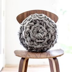 a gray and white knitted object sitting on top of a wooden chair in front of a window