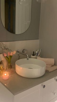 a white sink sitting under a bathroom mirror next to a vase with flowers in it