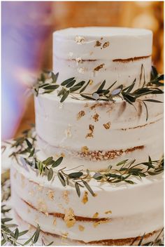 a three tiered white wedding cake with greenery on top and gold flakes