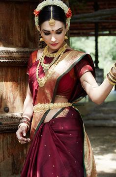 a woman in a purple and red sari with gold jewelry on her neck, smiling for the camera