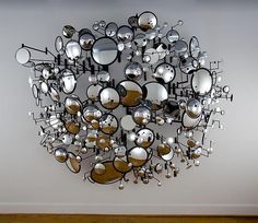 a circular mirror hanging on the wall with lots of silver objects in front of it