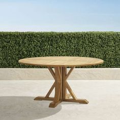 a wooden table sitting on top of a cement floor next to a green hedge covered wall