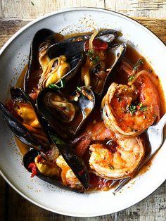 a white bowl filled with seafood and mussels on top of a wooden table