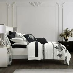 a white bed with black and white comforter on top of it next to a night stand