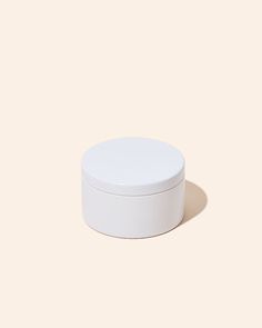 a white round container sitting on top of a beige surface with a shadow coming from it