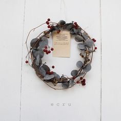 a wreath with leaves and berries hanging on the side of a white building that says ecru